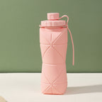Pink silicone folding bottle with packaging on a light surface and green background