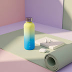 Gradient yellow to blue water bottle on a light surface with a blurred background